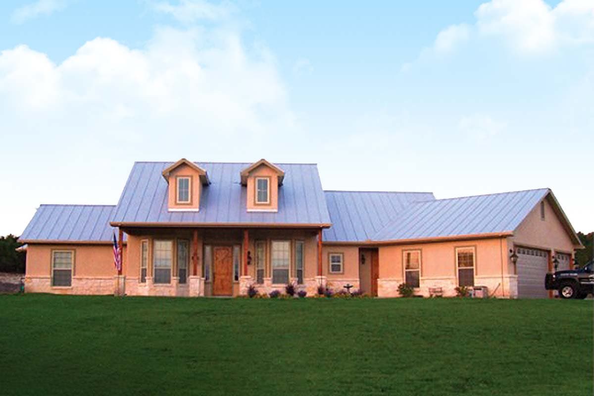 House plan exterior with metal roof, two dormers, covered porch with stone columns, and attached two-car garage.