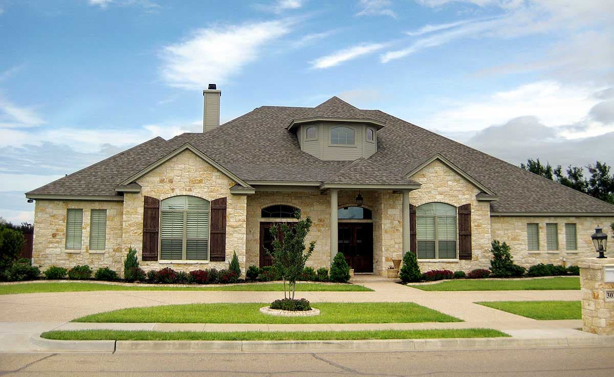House plan exterior: One-story stone house with prominent gables, arched windows, dormer, and covered entry.