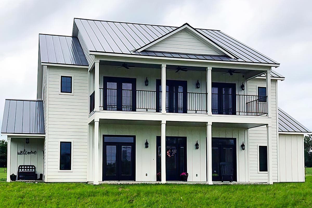 Two-story Modern Farmhouse plan with white siding, metal roofs, and a second-story balcony with black railings and French doors.