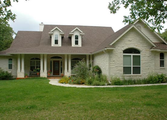 House plan exterior: One-story home with a covered porch, stone exterior, gable dormers, and arched window.