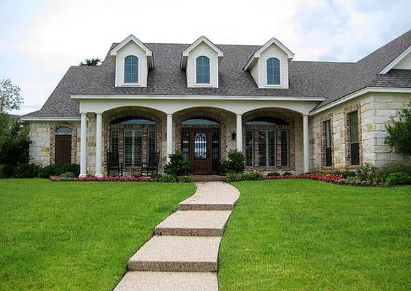 House plan exterior: Two-story home with stone accents, arched entry porch with columns, and three dormer windows.