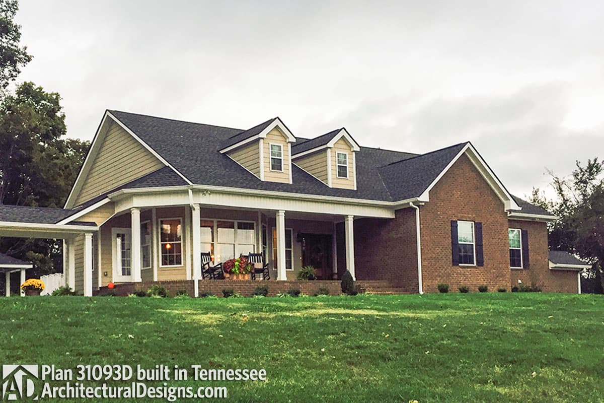 House plan exterior: One-story brick and vinyl home with wraparound porch, dormers, and attached carport.