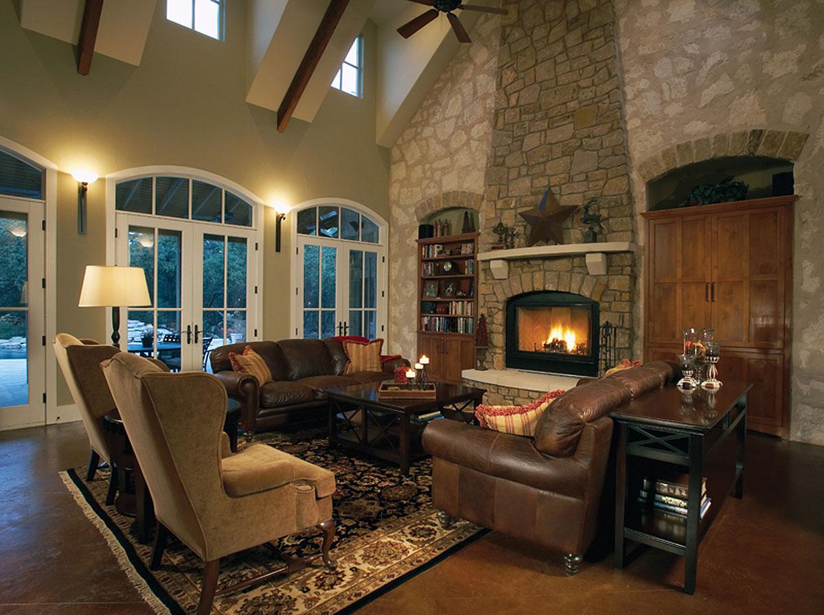 Interior view of great room with stone fireplace, vaulted beamed ceiling, large arched windows, and leather furniture.