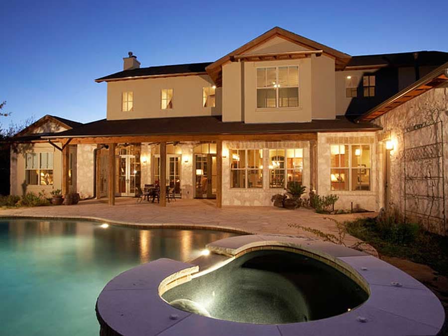 Two-story house exterior with a covered porch, multiple gables, stone accents, and a swimming pool.