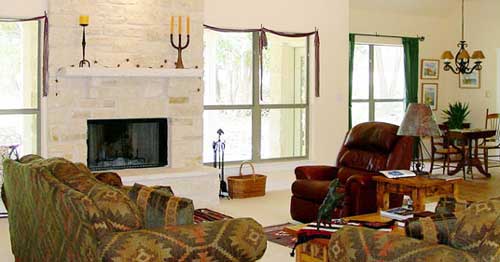 Living room interior with stone fireplace, patterned sofa, leather recliner, and dining area visible.