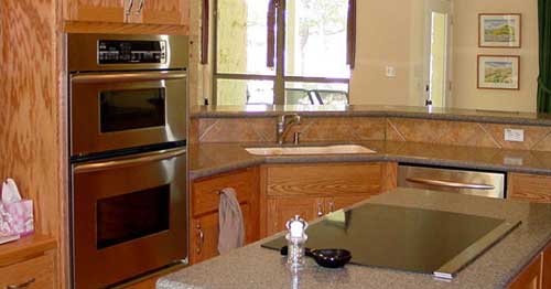 Kitchen interior with stainless steel double oven, granite countertops, island cooktop, sink, and dishwasher.