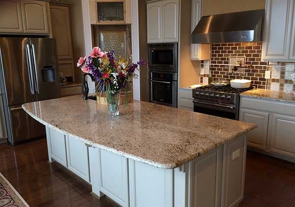 Kitchen with large granite island, stainless steel appliances, double oven, and range with tile backsplash.