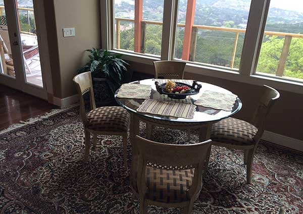 Dining nook with glass table, four chairs, and large windows overlooking a hillside view.