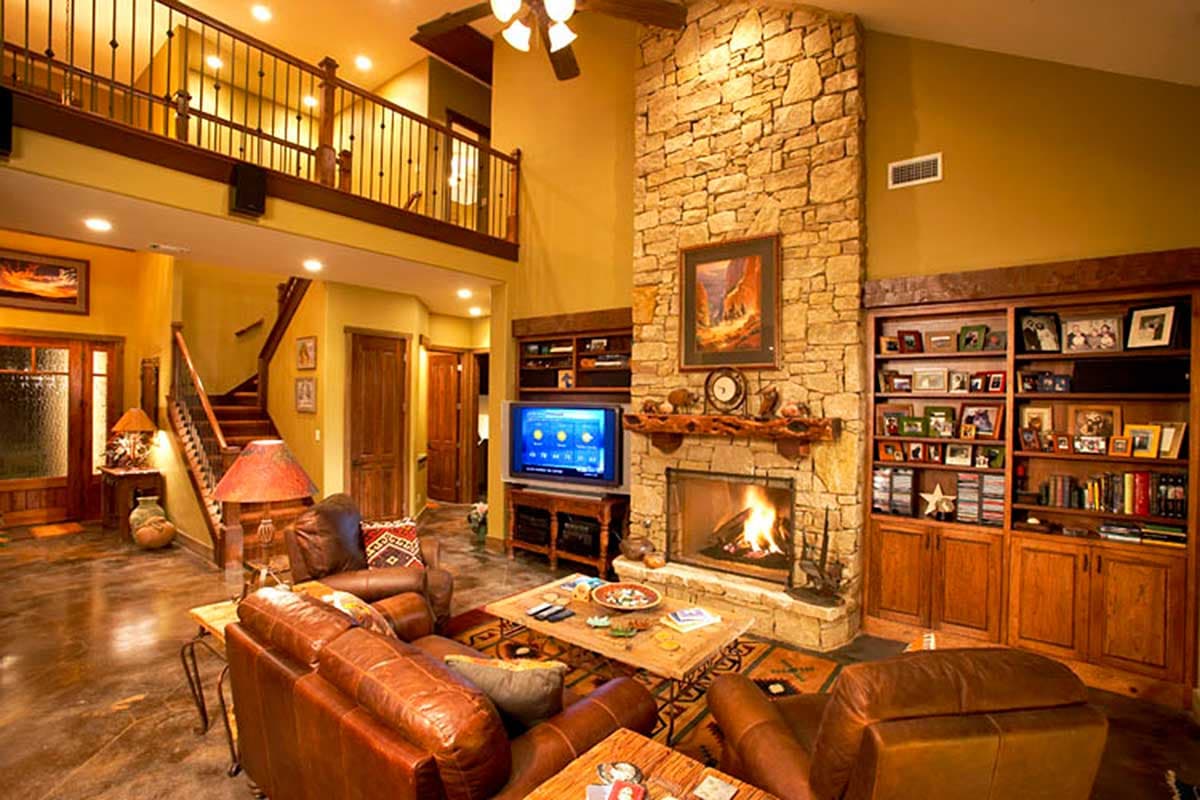 Living room with stone fireplace, built-in bookshelves, two-story loft, and leather furniture.