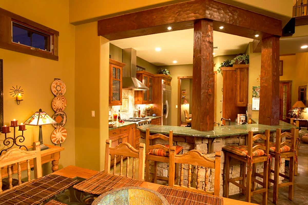 Interior view of a rustic kitchen and dining area with wood beams, stone accents, and a breakfast bar.