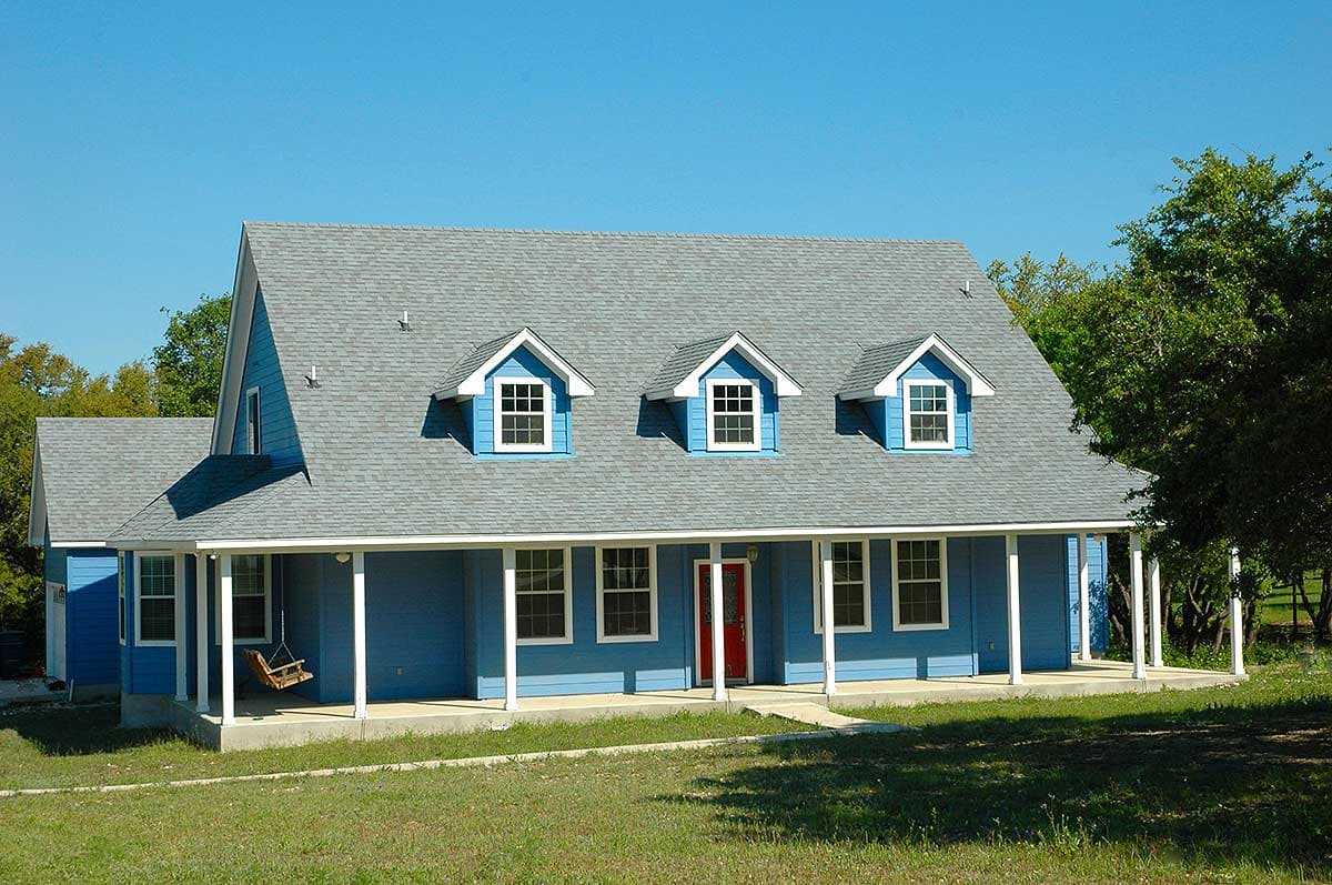 House plan exterior: Two-story home with wraparound porch, three gables with dormer windows, and a red front door.