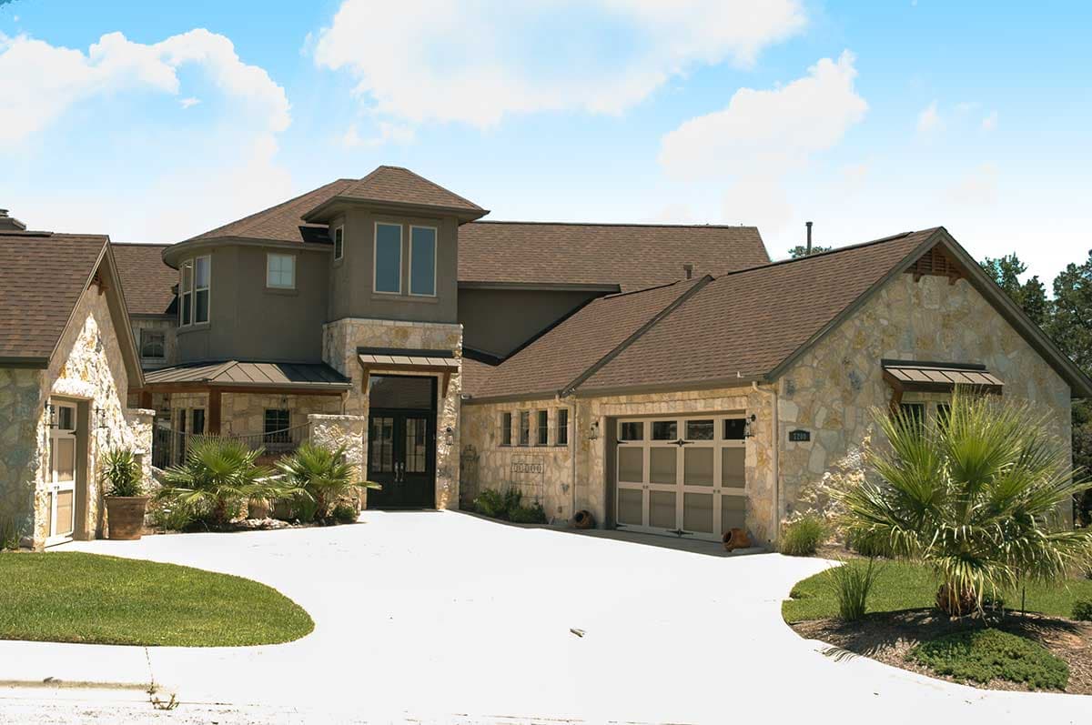 House plan exterior featuring stone and stucco, multi-level rooflines, double front doors, and a three-car garage.