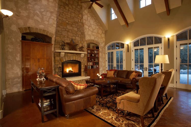 Great room with stone fireplace, built-in shelving, vaulted beamed ceiling, and large arched windows.