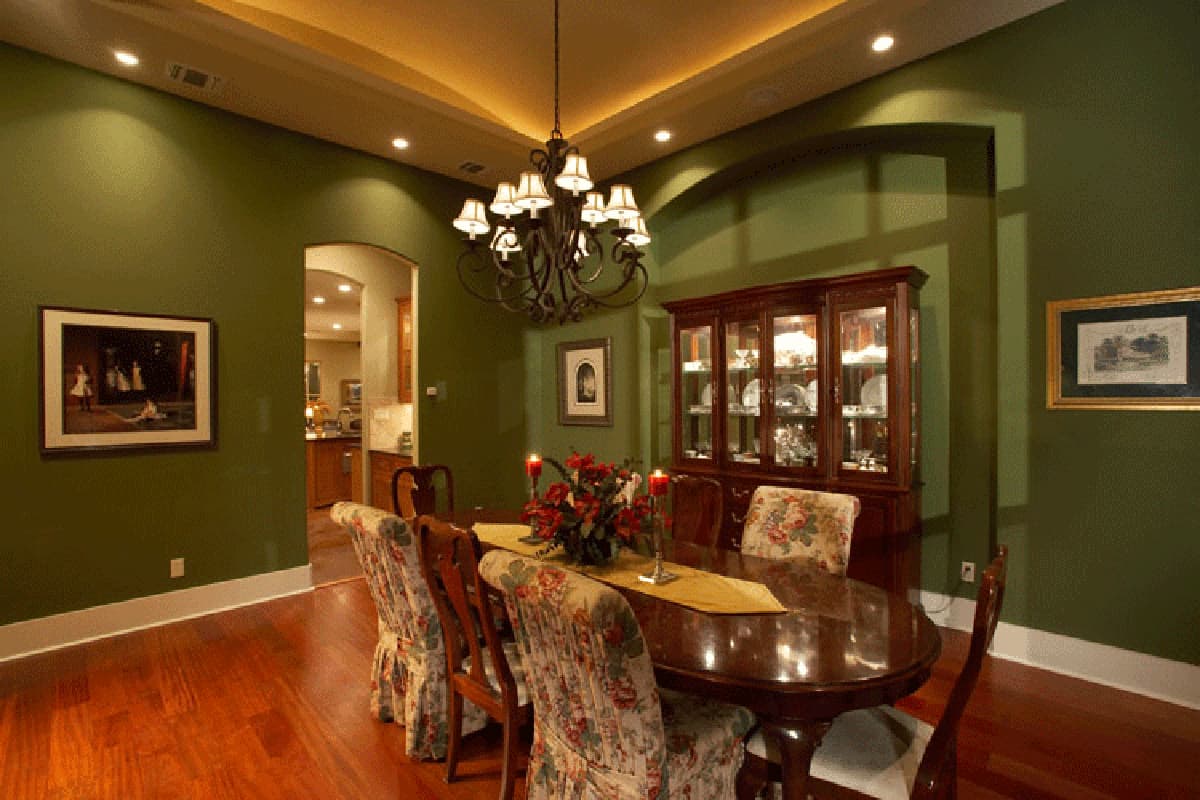 Dining room with oval table, upholstered chairs, buffet, chandelier, and arched entryway to kitchen.