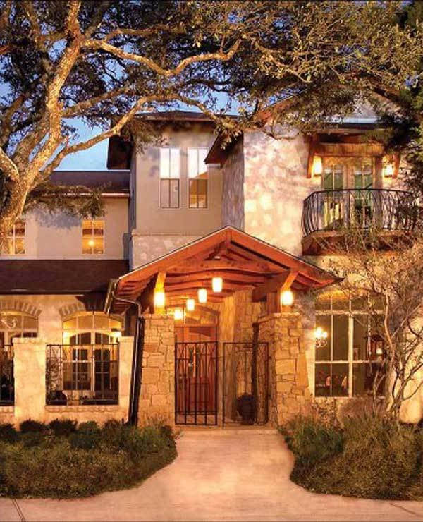 House plan exterior with stone entrance, wood-shingled roof, arched windows, and wrought-iron gate.