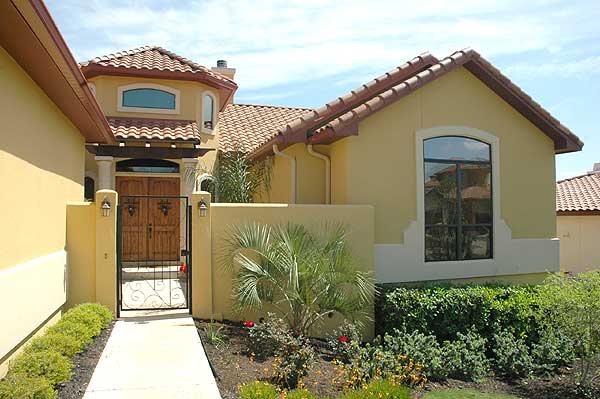 House plan exterior with arched windows, red tile roof, double wooden doors, and a metal gate leading to the entrance.