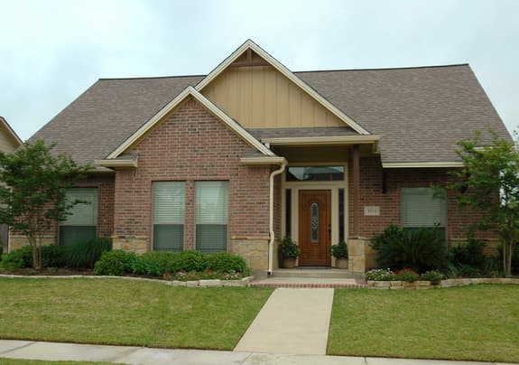 House plan exterior: Ranch style, brick facade with stone accents, prominent gabled dormer above entry, wide eaves.