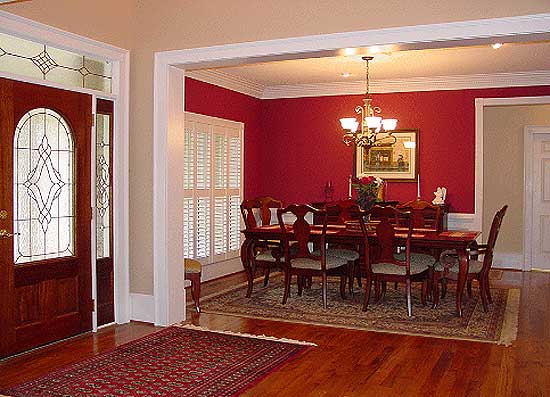 Interior view of a dining room with a large wooden table and chairs, a chandelier, and plantation shutters.