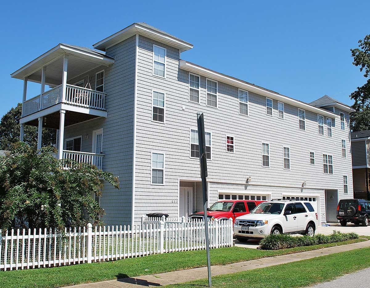 House plan exterior: Three-story building with stacked garages, covered balconies on second and third floors, and pale gray shingle siding.
