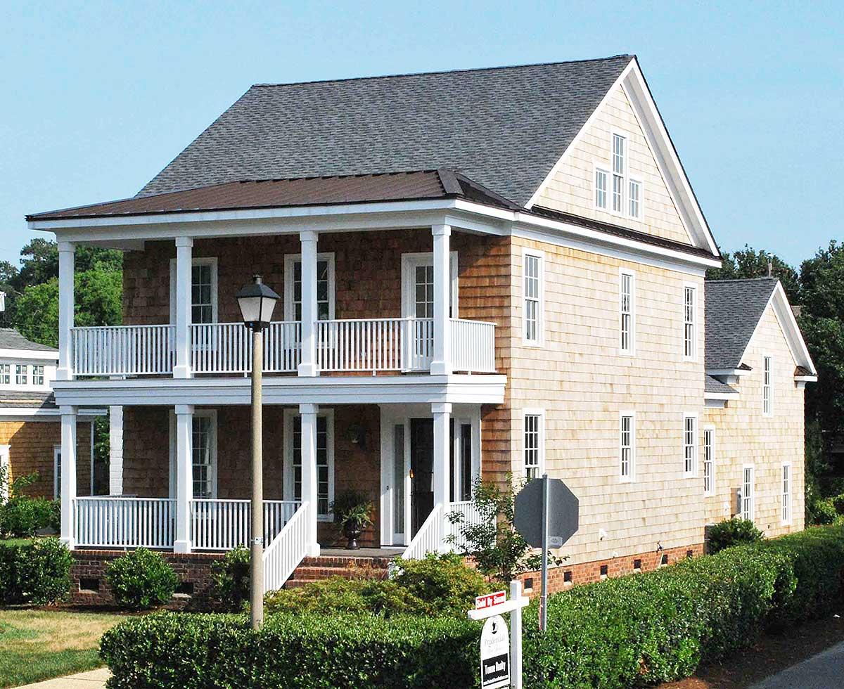 Two-story house plan exterior with double-tiered porches, white railings, cedar shake siding, and gabled dormers.