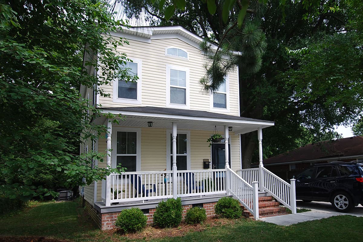 Two-story house plan exterior with a wrap-around porch, white railings, and arched dormer window.