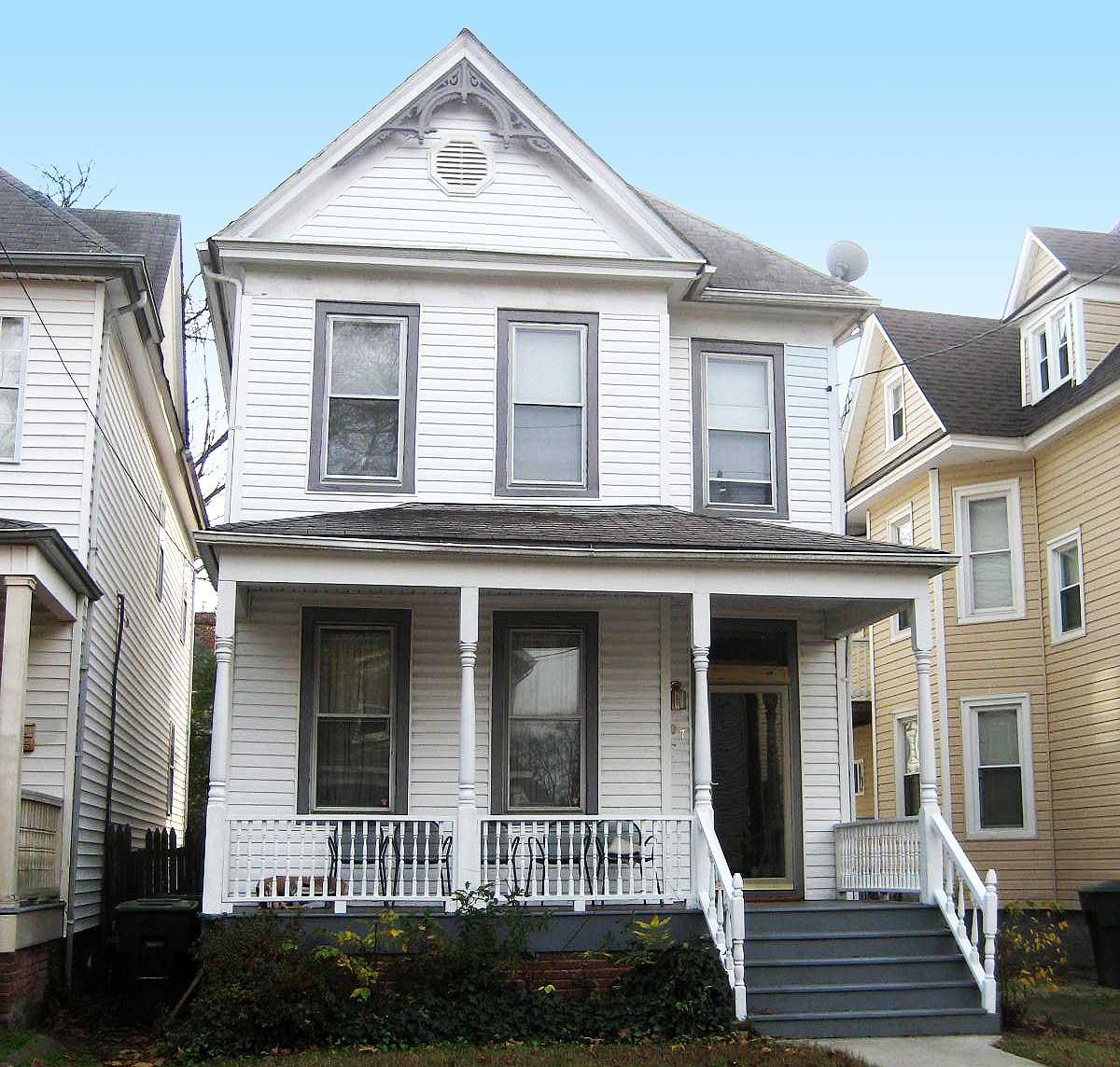 House plan exterior, two stories, white siding, full-width porch with decorative columns, gable with decorative vent.