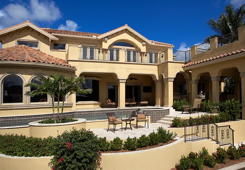 Two-story house plan exterior with Spanish tile roof, arched windows, balconies with ornate railings, and covered patio areas.