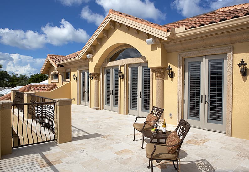 House plan exterior featuring a stucco finish, clay tile roof, arched entryway, and French doors with shutters.