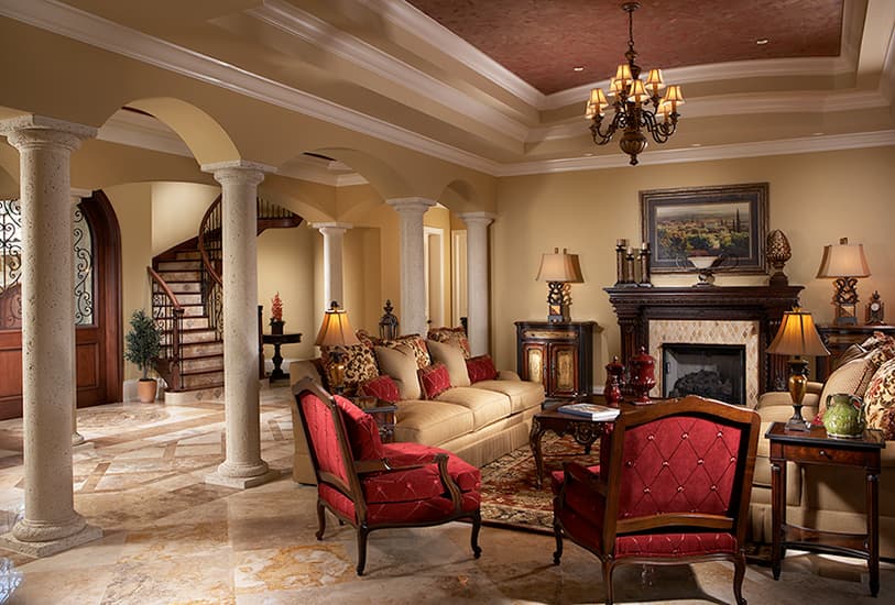 Interior view of a living room with a fireplace, ornate columns, and a spiral staircase. Features coffered ceiling.