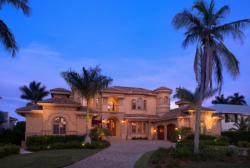 Mediterranean style house plan exterior, two stories, arched windows, turret details, tile roof, and a paved driveway.