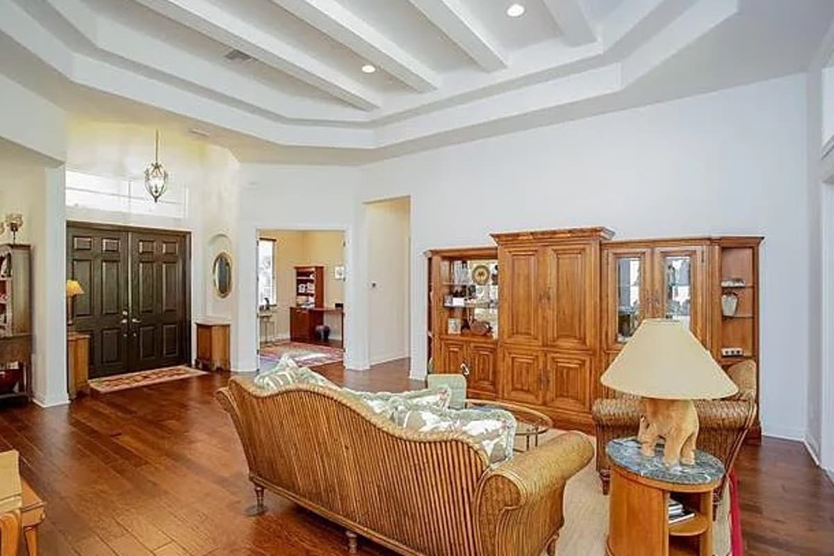 Interior view of a living room featuring coffered ceilings, double doors, large wooden cabinets, and a woven sofa.