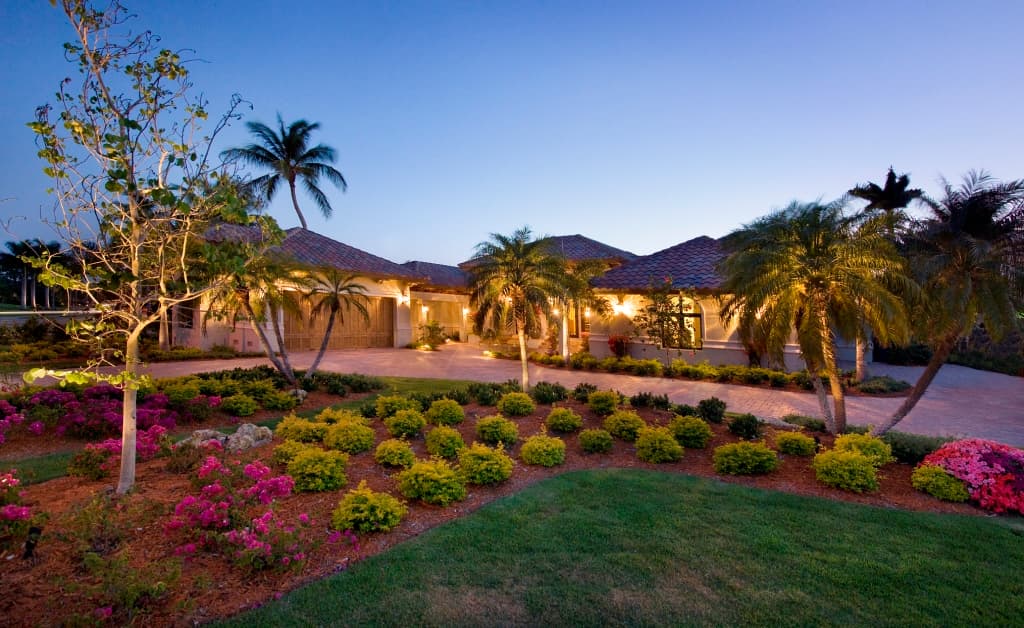 House plan exterior: Single-story residence with tile roof, attached garage, and illuminated landscaping.