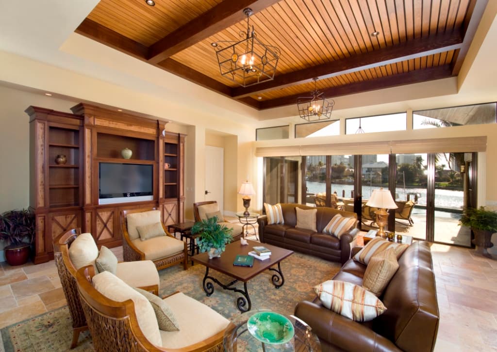 Living room with coffered wood ceiling, built-in entertainment center, leather sofas, and large windows overlooking water.