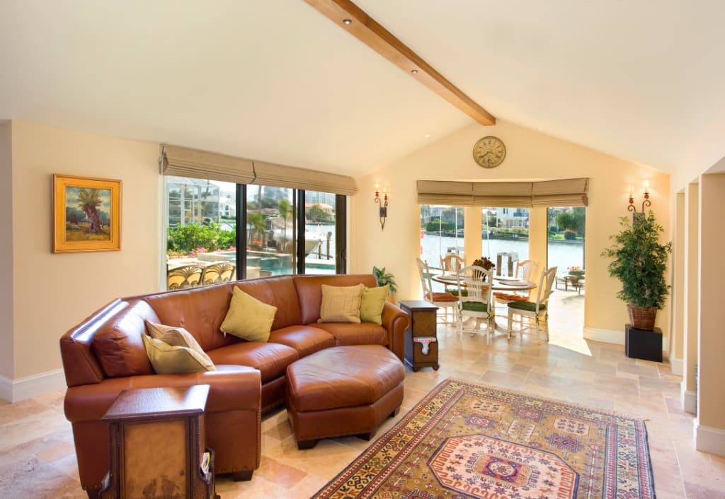 Interior view of a great room with vaulted ceiling, wood beam, sectional sofa, dining area, and water view.