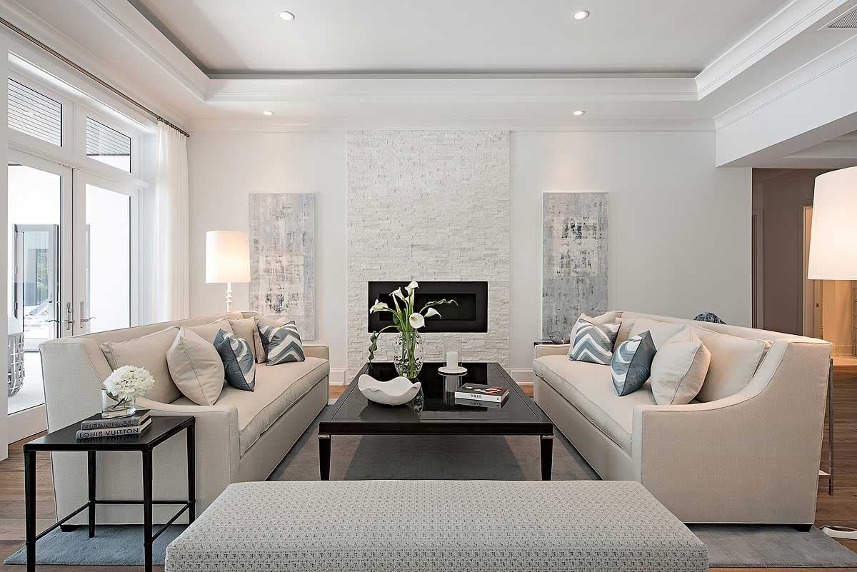 Living room with a white stone fireplace, two sofas, and glass doors leading outside. Tray ceiling with recessed lighting.