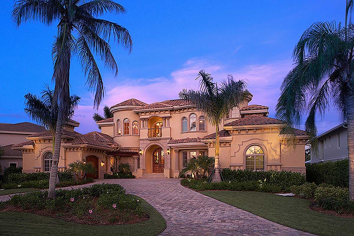 House plan exterior: large Mediterranean-style residence with arched windows, tile roof, balcony, and porte-cochère.