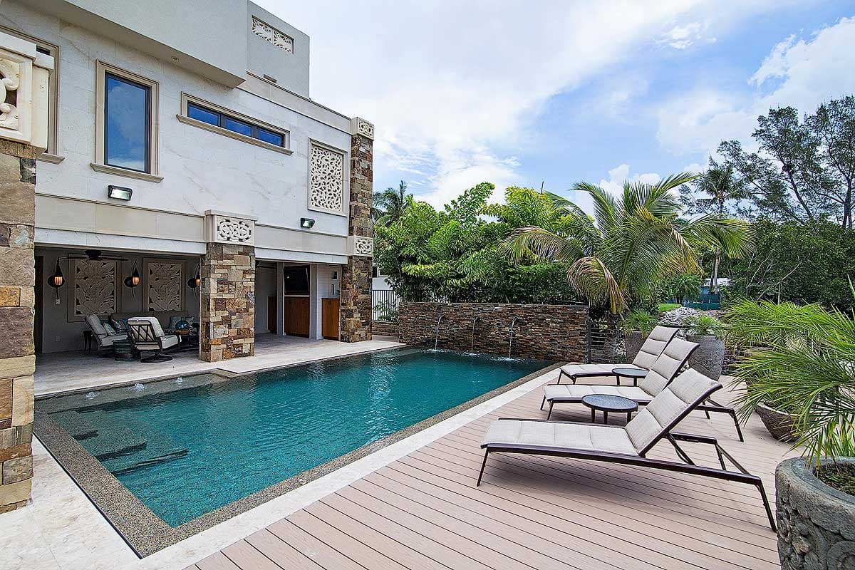 Modern house exterior with lap pool, stone pillars, open patio seating, and water feature.