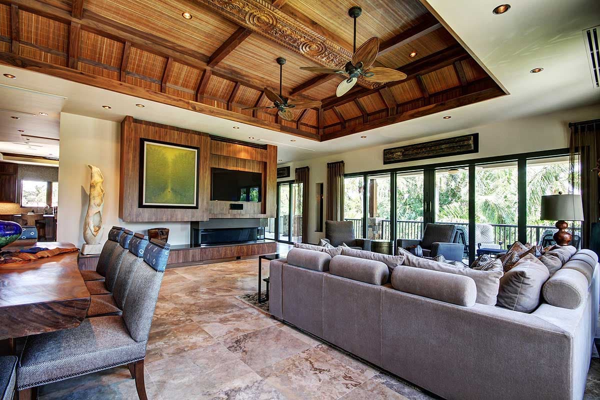 Living room with coffered wood ceiling, fireplace, large sofa, and floor-to-ceiling windows with balcony access.