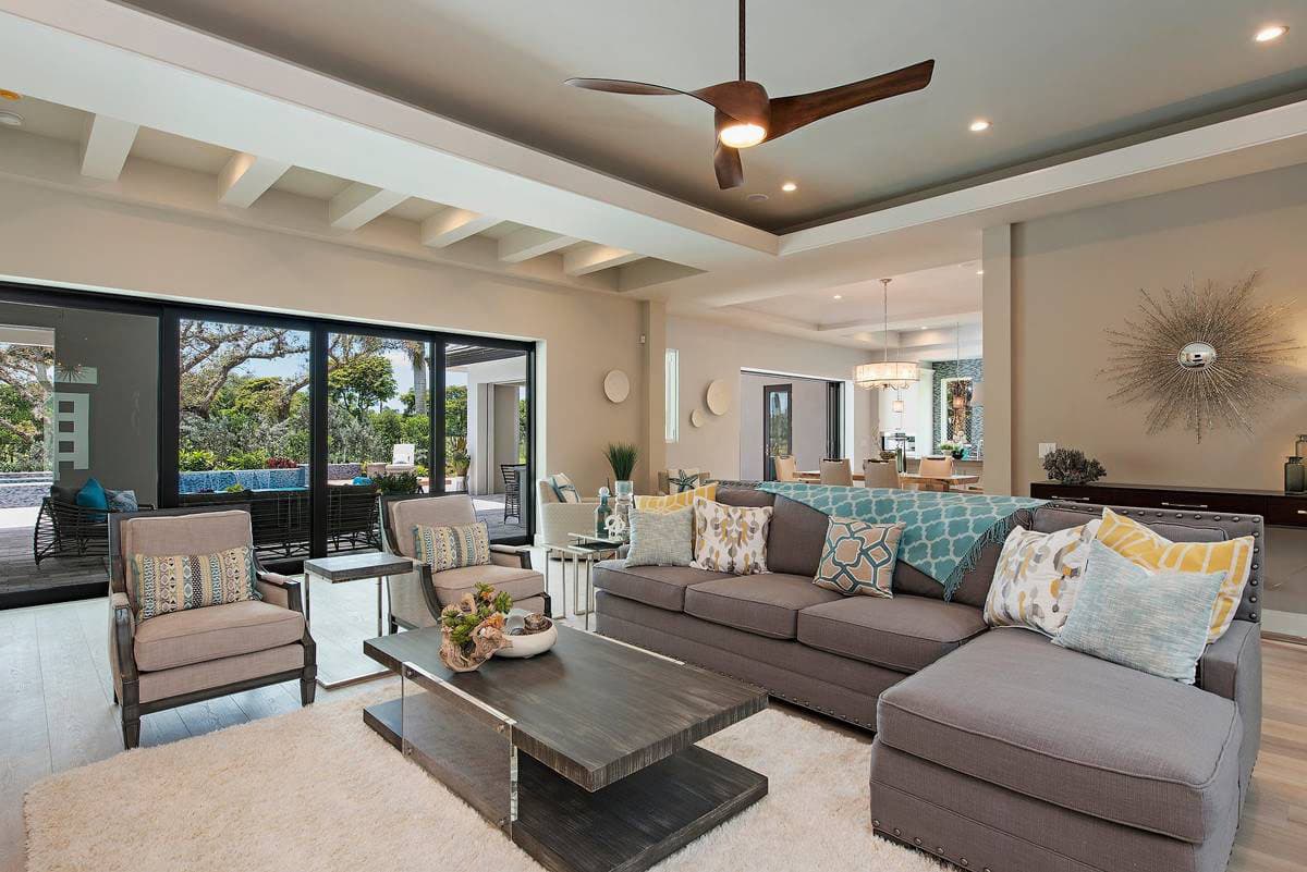 Living room interior with sectional sofa, coffee table, and view to patio through sliding glass doors. Coffered ceiling with fan.