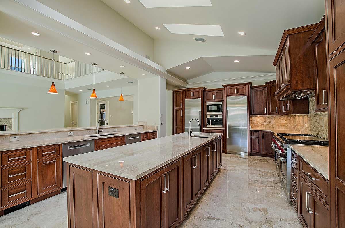 Kitchen with large island, stainless steel appliances, dark wood cabinetry, granite countertops, and vaulted ceiling with skylights.
