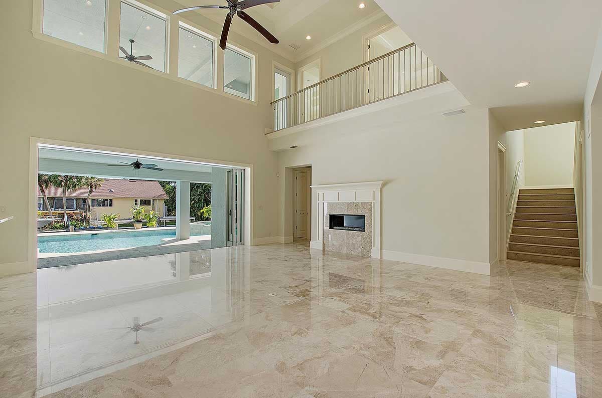 Interior view of a great room with a fireplace, two-story ceiling, upper-level balcony, and large sliding doors to a pool area.