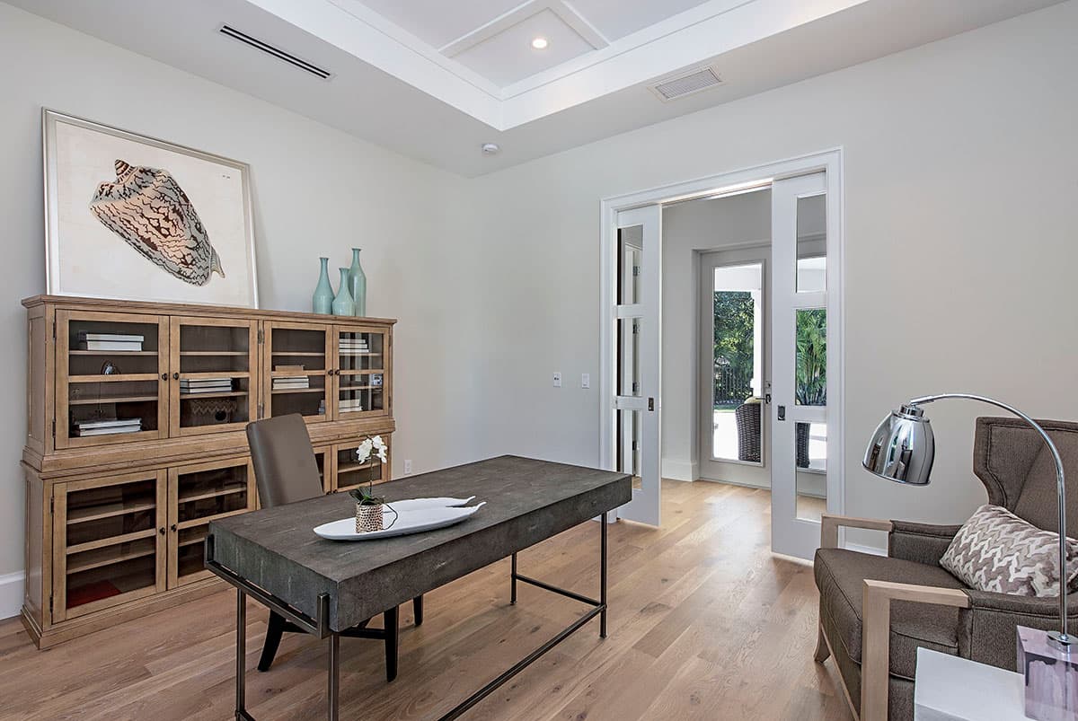 Home office with glass-paneled sliding doors, a large desk, a wooden cabinet with glass doors, and a comfortable armchair.