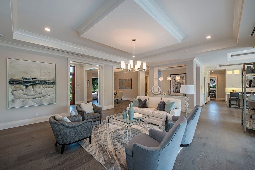 Open-concept living area with tray ceiling, sectional sofa, glass coffee table, and view into dining room and kitchen.