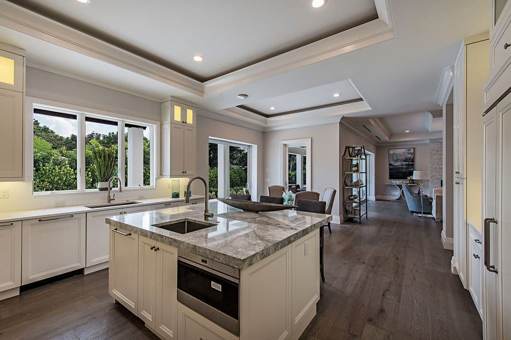 Modern kitchen with island, marble countertops, stainless steel appliances, and a sink overlooking a large window.