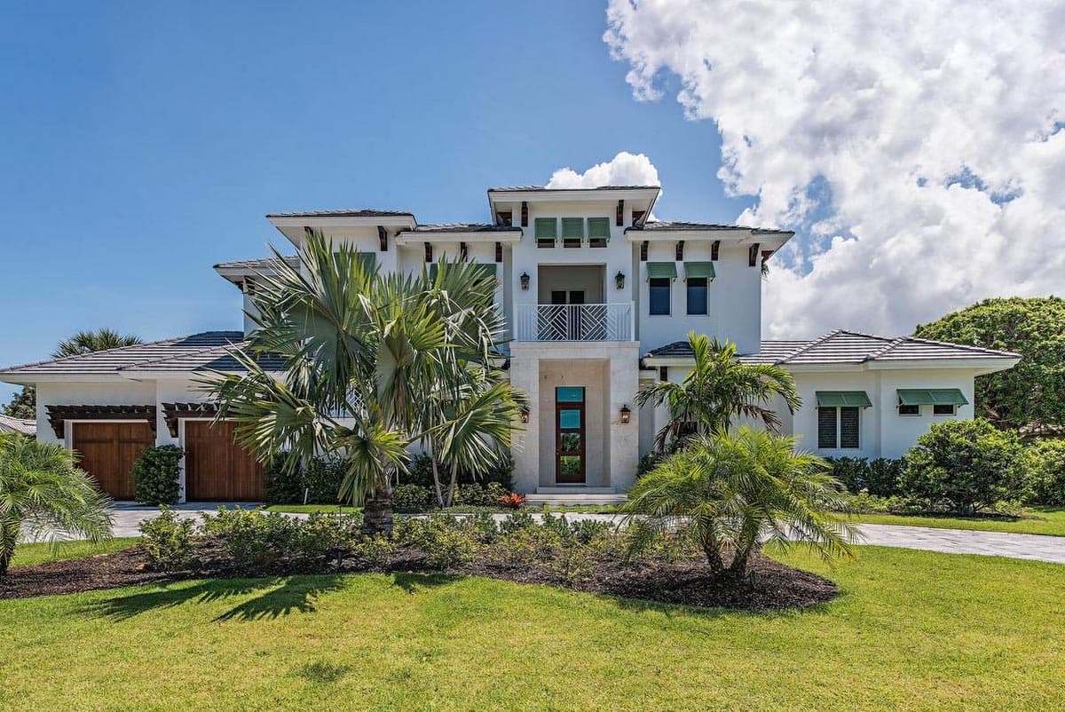 House plan exterior. Two-story home with a flat roof, balcony, and garage with wood doors. Features include decorative brackets and green awnings.