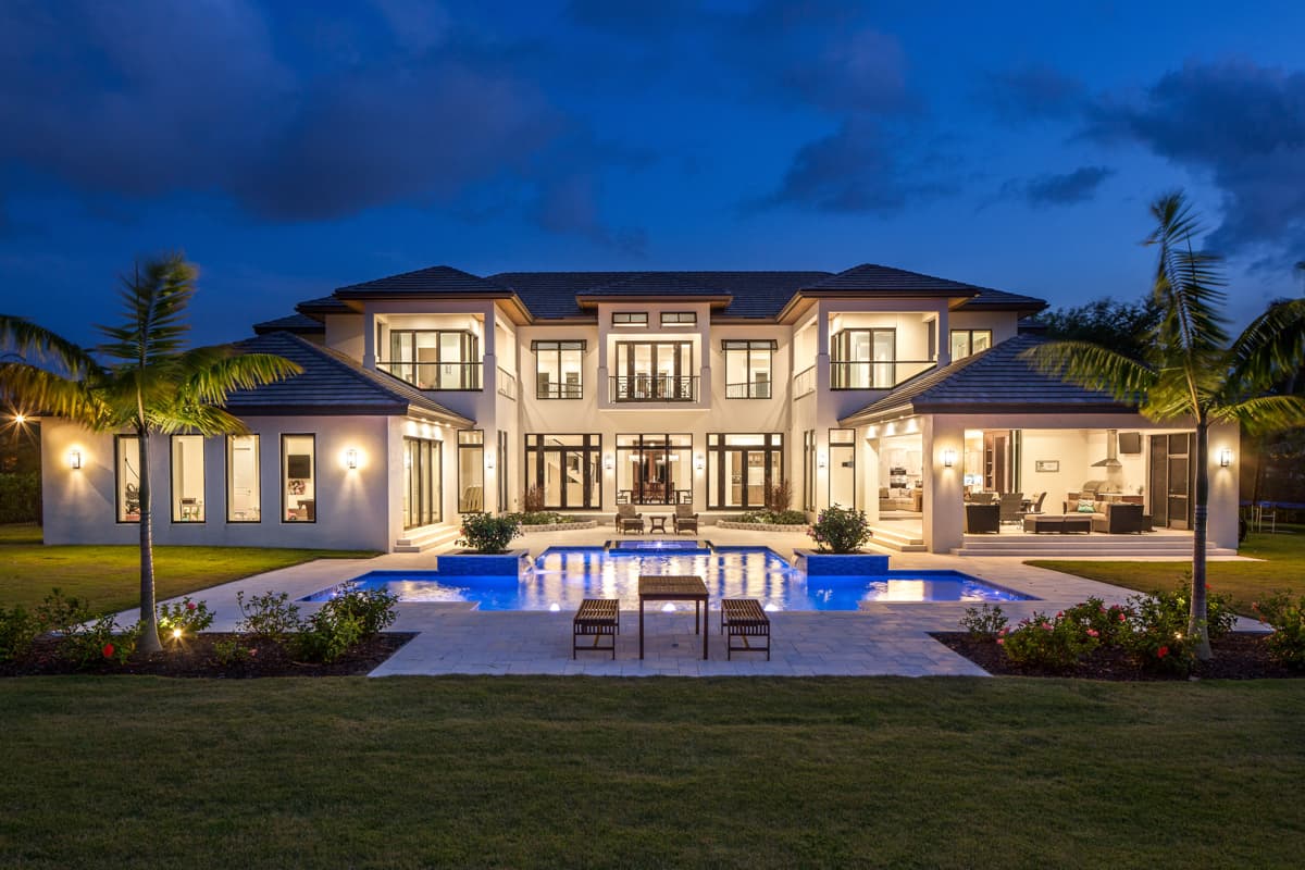 Modern two-story house plan exterior with a U-shaped pool, covered outdoor living area with kitchen, and extensive glazing.