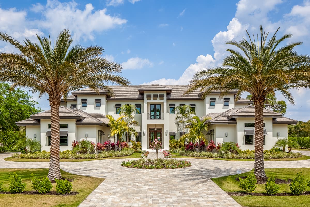 Modern house plan exterior, two stories, with central entrance balcony, low-pitch hip roofs, and paved circular driveway.