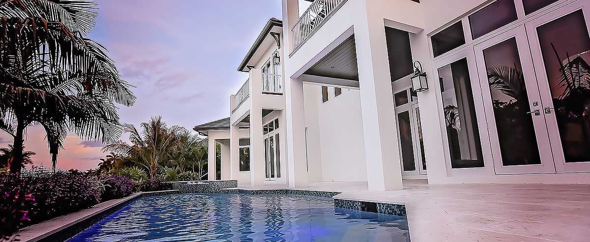 Modern two-story house exterior with balconies, large windows, white columns, and a swimming pool.
