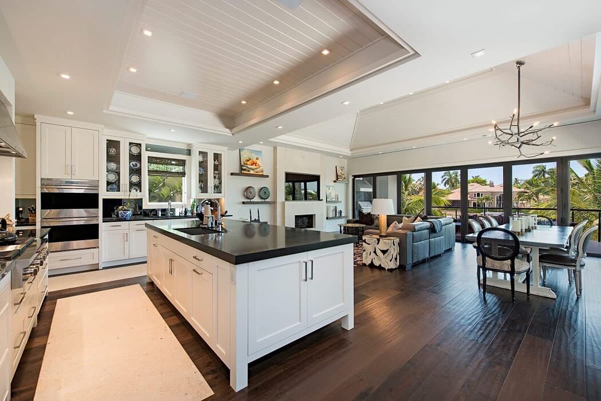 Open-concept kitchen and living area with large island, fireplace, and expansive windows overlooking palm trees.