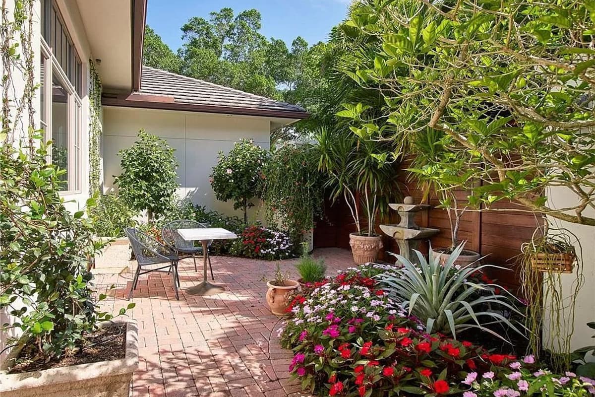 Courtyard with brick patio, fountain, potted plants, and lush flowering ground cover.